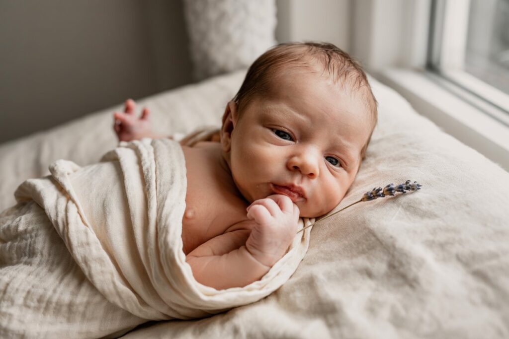Newborn baby showing an early hunger cue by bringing their hand towards their mouth.